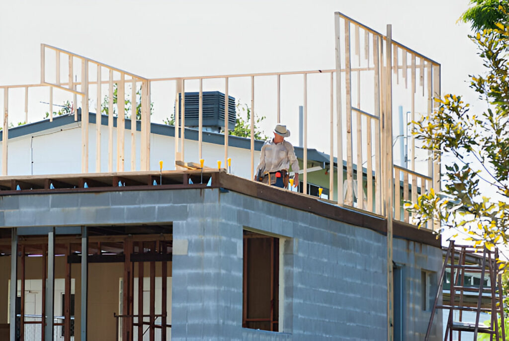 Construction worker standing on the second floor of a building under construction, with wooden framing being installed above a concrete block structure