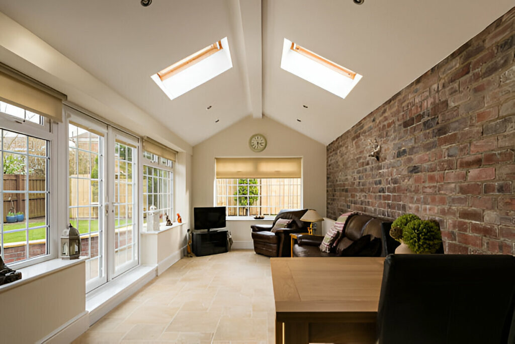 Bright sunroom with large windows, skylights, exposed brick wall, and cozy seating area