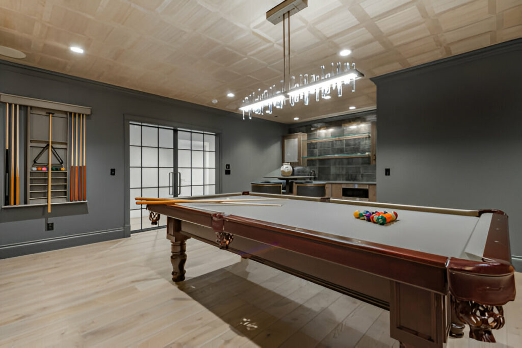 Modern game room featuring a classic pool table, sleek gray walls, a built-in bar area, and a stylish chandelier