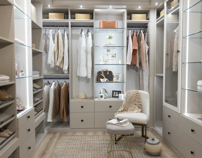 A sophisticated walk-in closet featuring organized shelves, hanging rods, and drawers in neutral colors, with a cozy chair and decorative elements