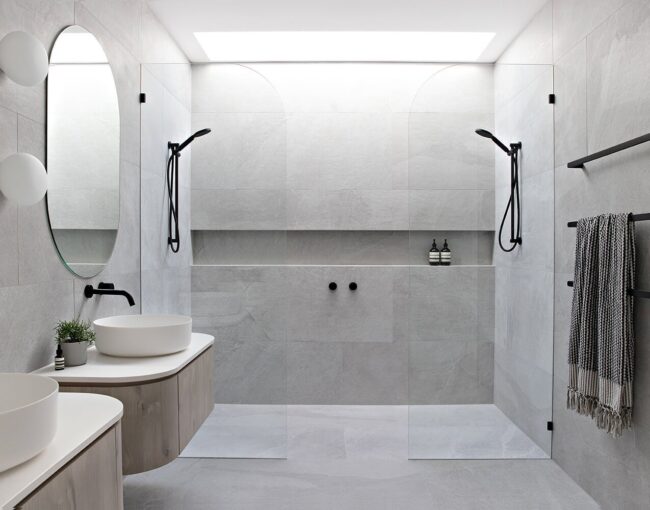 Modern Scandinavian bathroom featuring double walk-in showers, floating vanities, round mirrors, and matte black fixtures