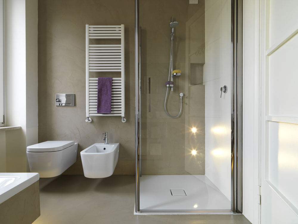 The image shows a spacious, well-lit bathroom with a walk-in shower, toilet, and vanity. The room features a clean, minimalist design with neutral colors and high-end fixtures.