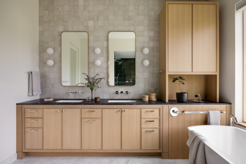 Custom Cabinetry Trends for Bathrooms to Watch in 2025 15 Bathroom featuring light wood cabinetry, black countertops, dual rectangular mirrors, and soft tile backsplash