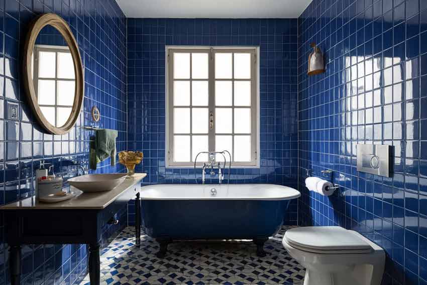 Custom Cabinetry Trends for Bathrooms to Watch in 2025 9 Vintage-style bathroom featuring glossy navy blue wall tiles, a deep blue freestanding tub, patterned mosaic floor, and wooden framed mirror