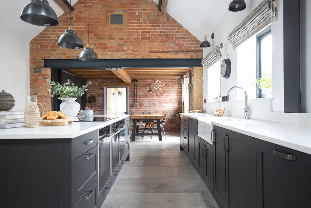 Top Kitchen Flooring Trends for 2025 6 Industrial-style kitchen featuring grey tumbled porcelain stone floors, matte black cabinetry, white countertops, and exposed red brick walls with black-framed windows and industrial pendant lighting.