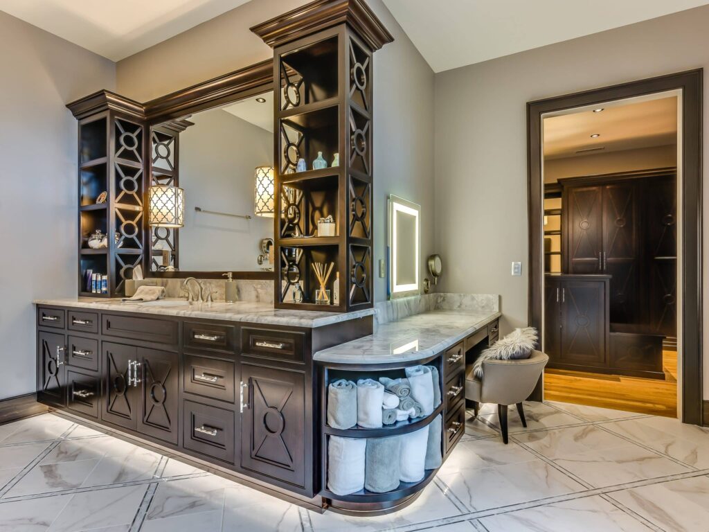 Custom Cabinetry Trends for Bathrooms to Watch in 2025 14 Luxurious bathroom featuring custom dark wood cabinetry, marble countertops, built-in vanity lights, and a cozy makeup station