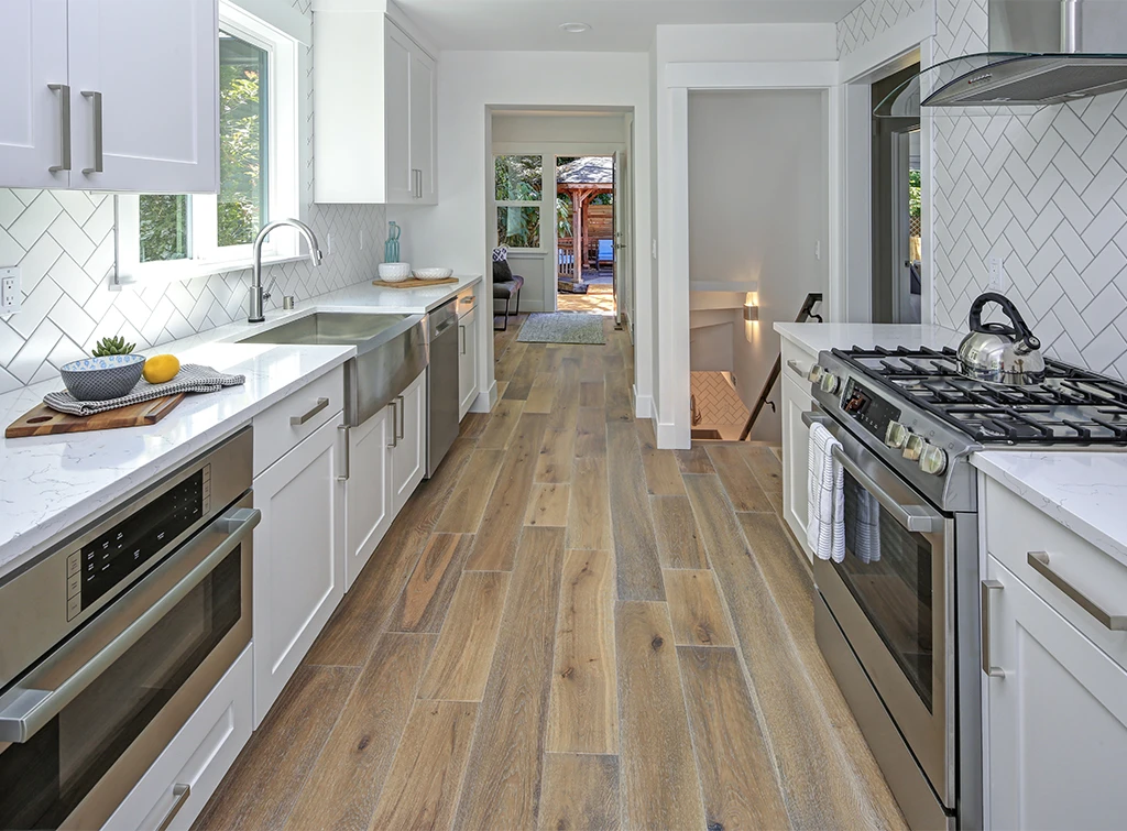 Creative Kitchen Floor Ideas 12 Contemporary galley kitchen with white cabinetry, stainless steel appliances, and wood-look tile flooring in a natural finish.