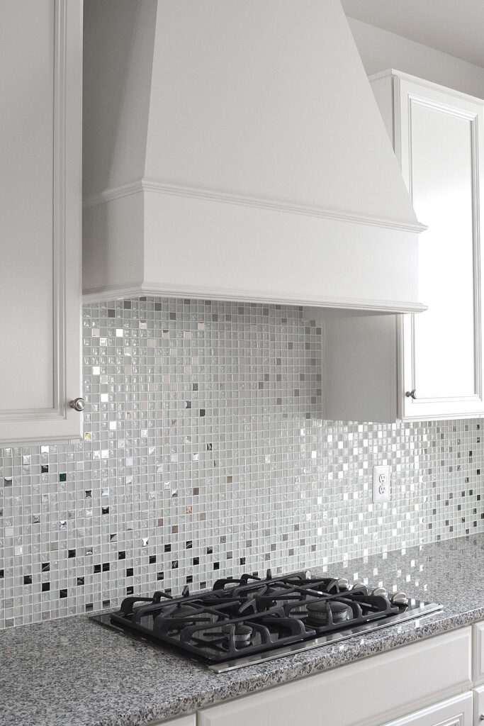 Modern Kitchen Backsplash Ideas in Alide, VA 9 Close-up of a white kitchen featuring a glass and metal mosaic backsplash and a gas stovetop