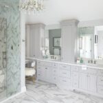 Luxurious master bathroom with gray cabinetry, marble tile floors, built-in vanity space, and a frameless glass shower enclosure.