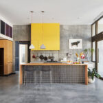 Contemporary kitchen with concrete floors, yellow upper cabinets, wood accents, and large glass doors