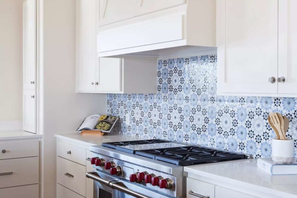 Modern Kitchen Backsplash Ideas in Alide, VA 13 Modern white kitchen featuring a patterned blue Moroccan tile backsplash, stainless steel stove with red knobs, and white cabinetry