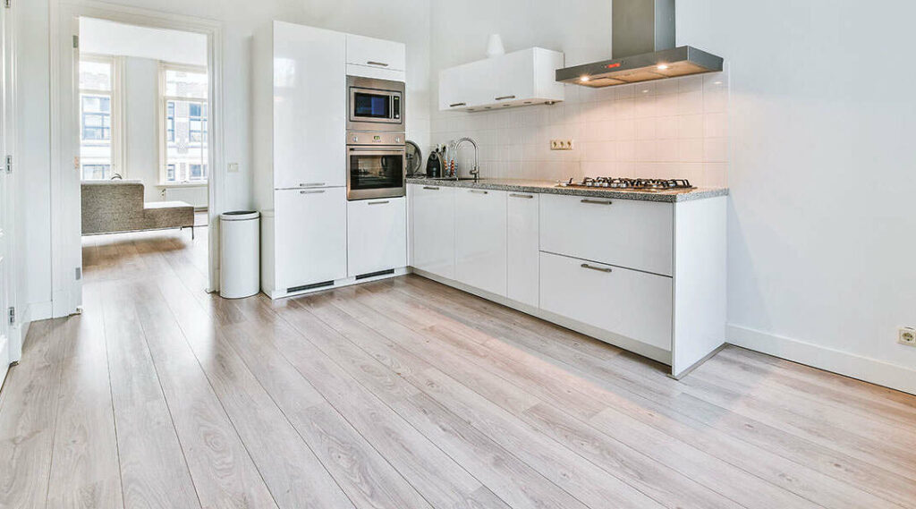 Best Kitchen Flooring Options 13 Minimalist kitchen with white cabinets, stainless steel appliances, and light laminate wood flooring