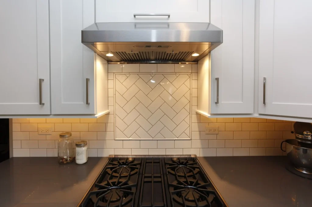 Modern Kitchen Backsplash Ideas in Alide, VA 14 Modern white kitchen with a classic subway tile backsplash featuring a herringbone pattern focal point behind a stainless steel range hood