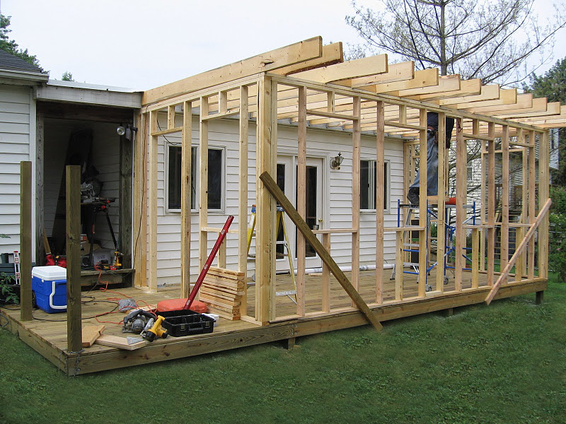 Construction of a home addition showing wood framing, roof joists, and tools on a deck