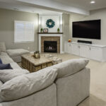 Finished basement featuring a large sectional sofa, rustic wood coffee table, brick fireplace, and wall-mounted TV