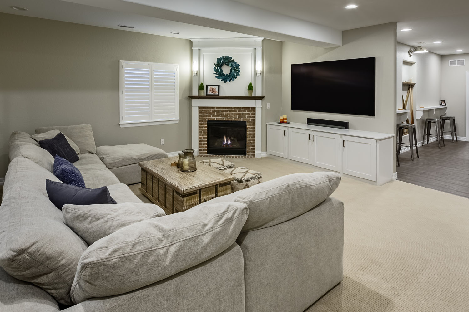 Finished basement featuring a large sectional sofa, rustic wood coffee table, brick fireplace, and wall-mounted TV