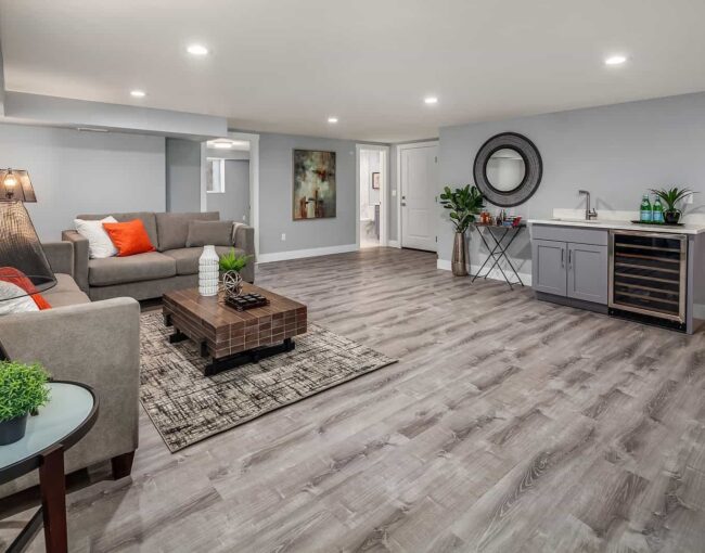 Stylish finished basement featuring gray wood flooring, cozy seating area, coffee table, and wet bar with wine fridge