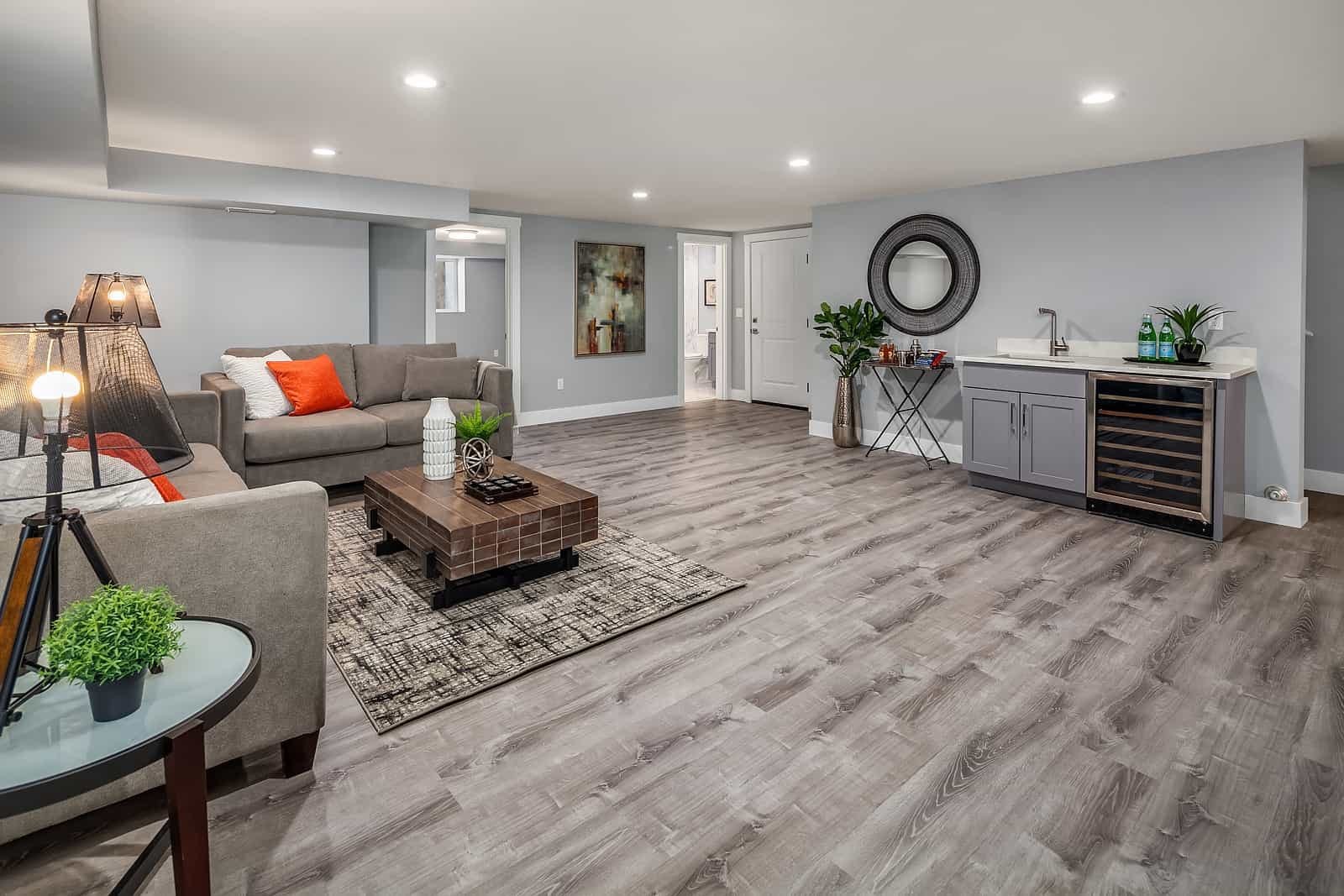 Stylish finished basement featuring gray wood flooring, cozy seating area, coffee table, and wet bar with wine fridge