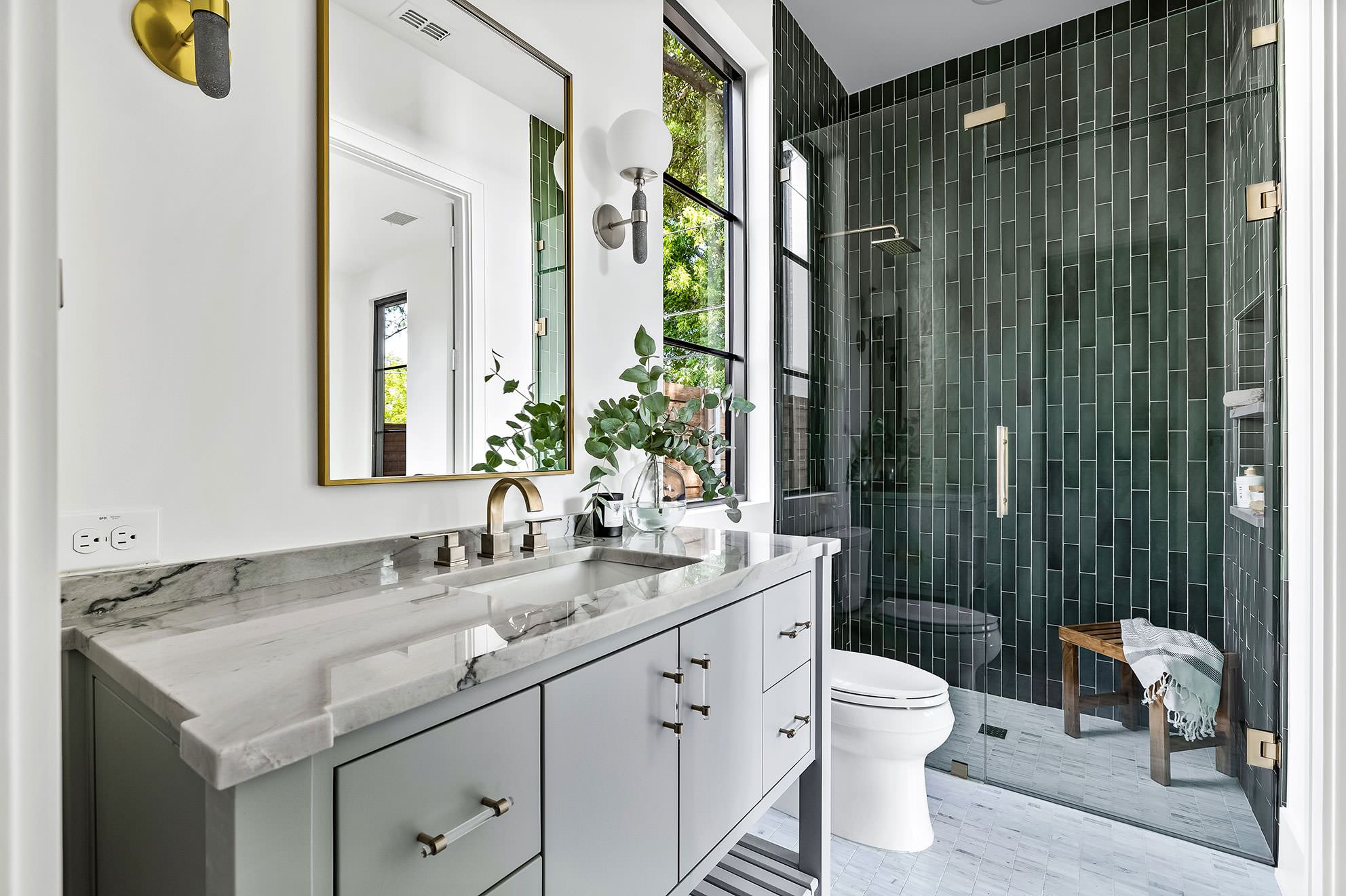 Modern bathroom with marble vanity and dark green tiled shower.
