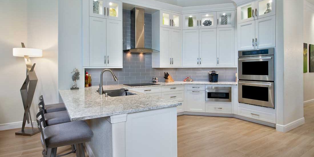 Modern kitchen featuring white cabinets, granite countertops, gray subway tile backsplash, and built-in stainless steel ovens