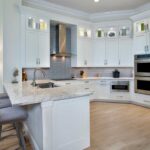 Modern kitchen featuring white cabinets, granite countertops, gray subway tile backsplash, and built-in stainless steel ovens