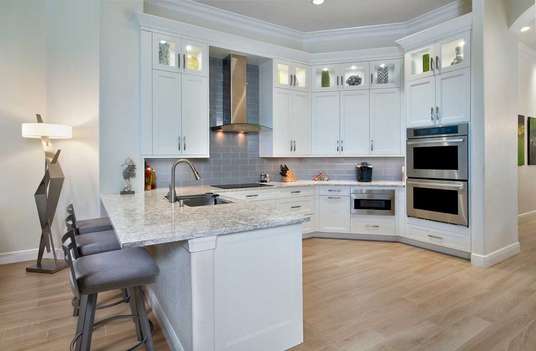Modern kitchen featuring white cabinets, granite countertops, gray subway tile backsplash, and built-in stainless steel ovens