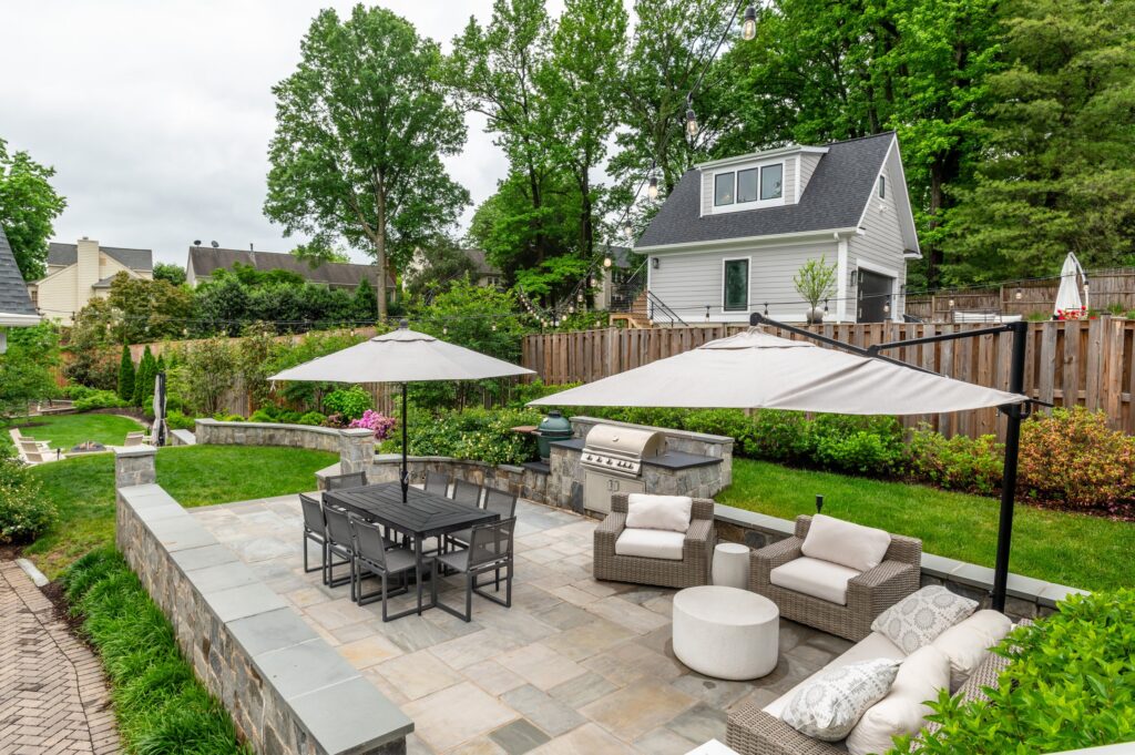 Backyard patio with outdoor kitchen, dining area, and wicker lounge seating under umbrellas