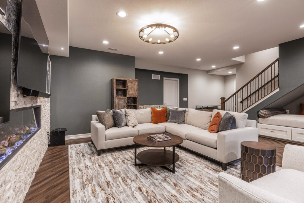 Inviting basement featuring stone fireplace with mounted TV, large sectional sofa with colorful pillows, and wood floors