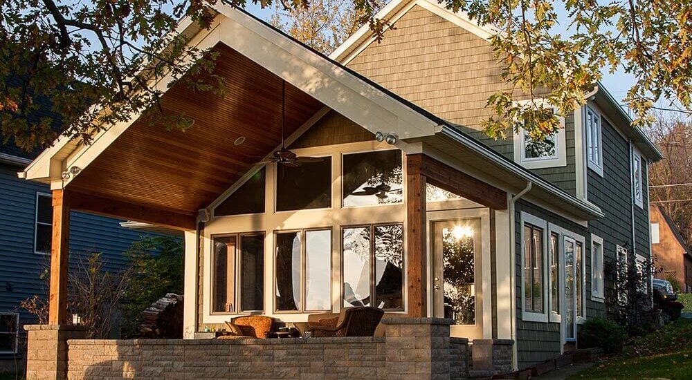 Two-story house with green siding featuring a modern addition with large windows and a covered patio