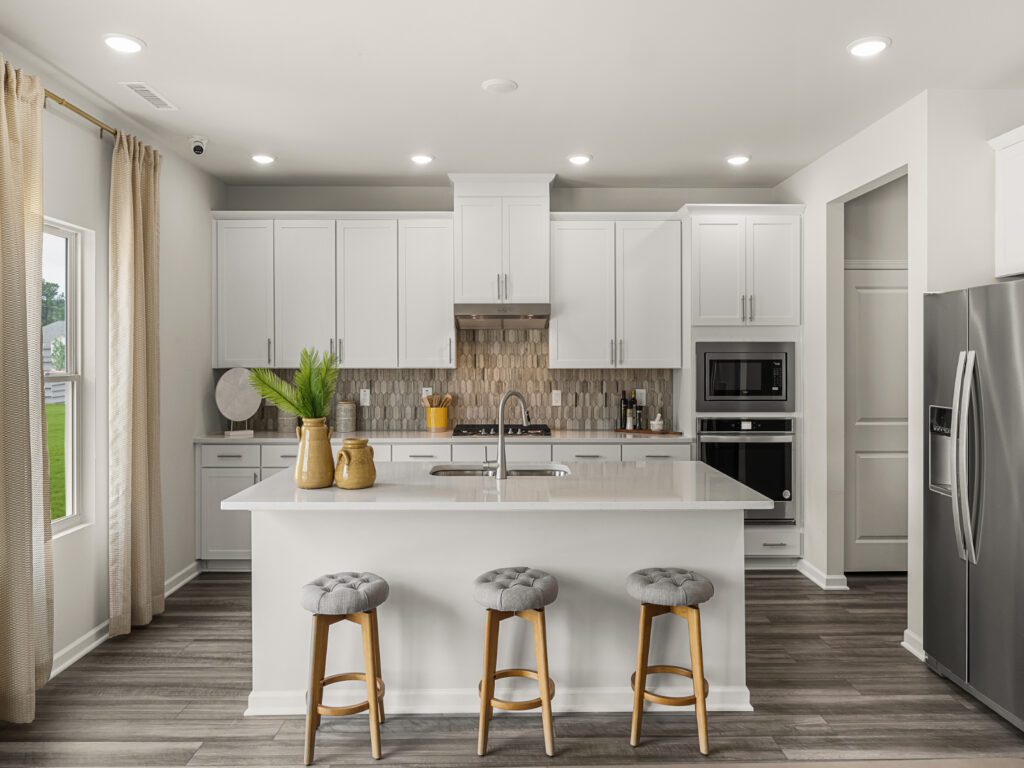 Contemporary white kitchen featuring quartz island, neutral backsplash, stainless steel appliances, and light wood flooring