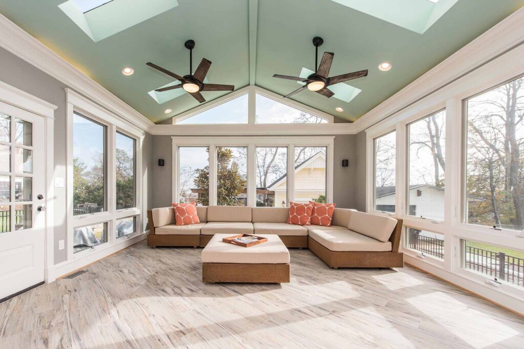 Spacious sunroom with large windows, vaulted ceiling with skylights, modern ceiling fans, and light wood flooring