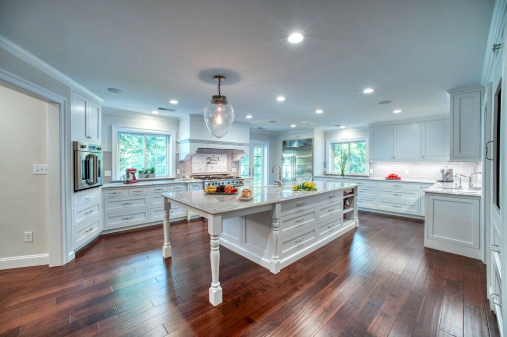 Spacious luxury kitchen with white cabinetry, marble island, and hardwood floors