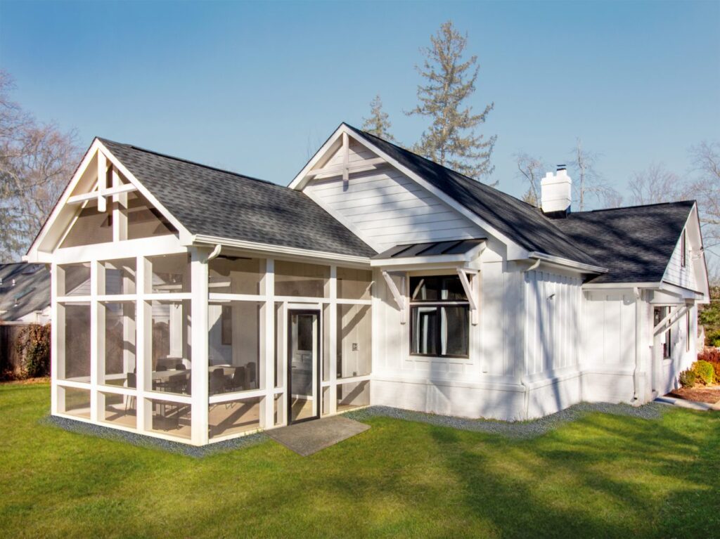 White house with black roof featuring a screened porch addition and spacious green lawn