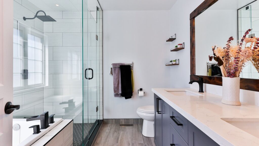 Modern bathroom with glass shower, wood-look floors, double vanity, and decorative wall shelves
