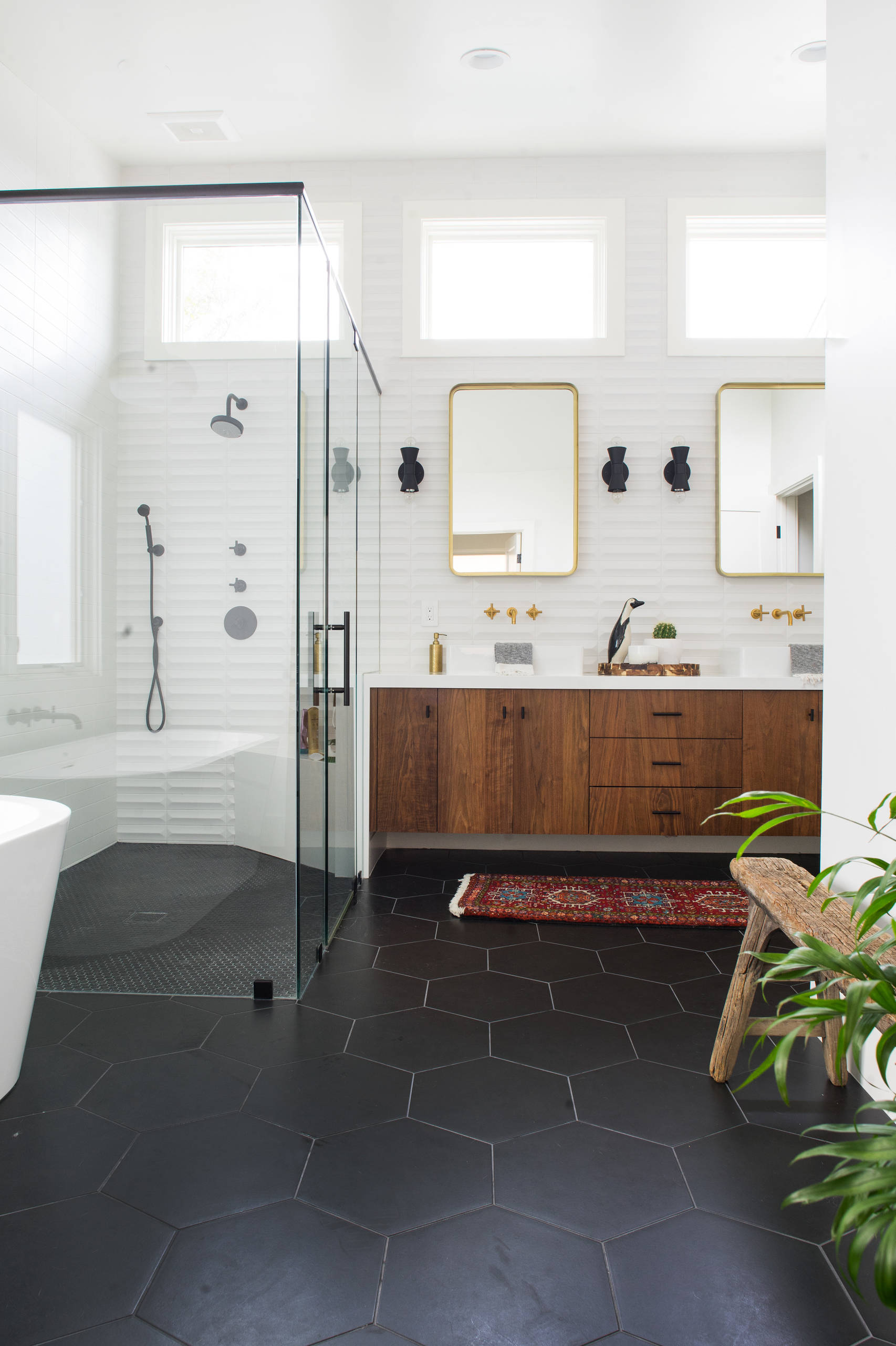 Modern bathroom with glass shower, wooden vanity, and black hexagon tile floor.