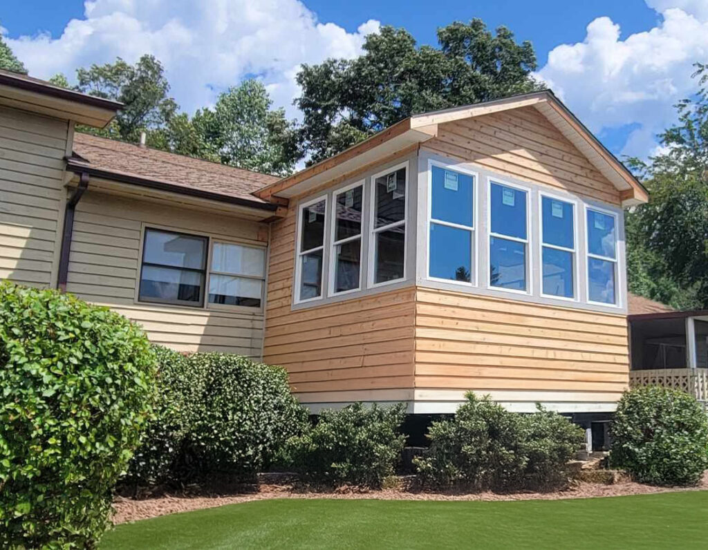 House extension featuring natural wood siding, multiple large windows, and landscaped shrubs