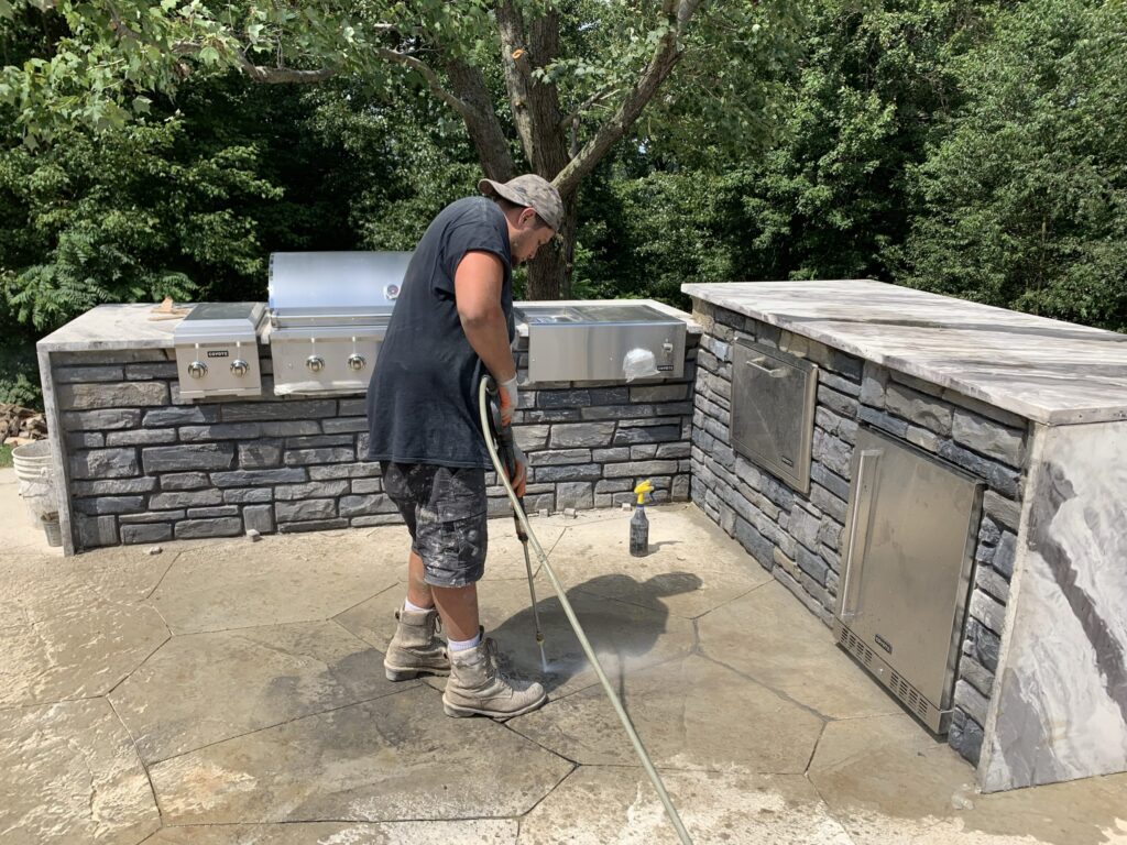  Man cleaning outdoor stone kitchen area with built-in grills and appliances