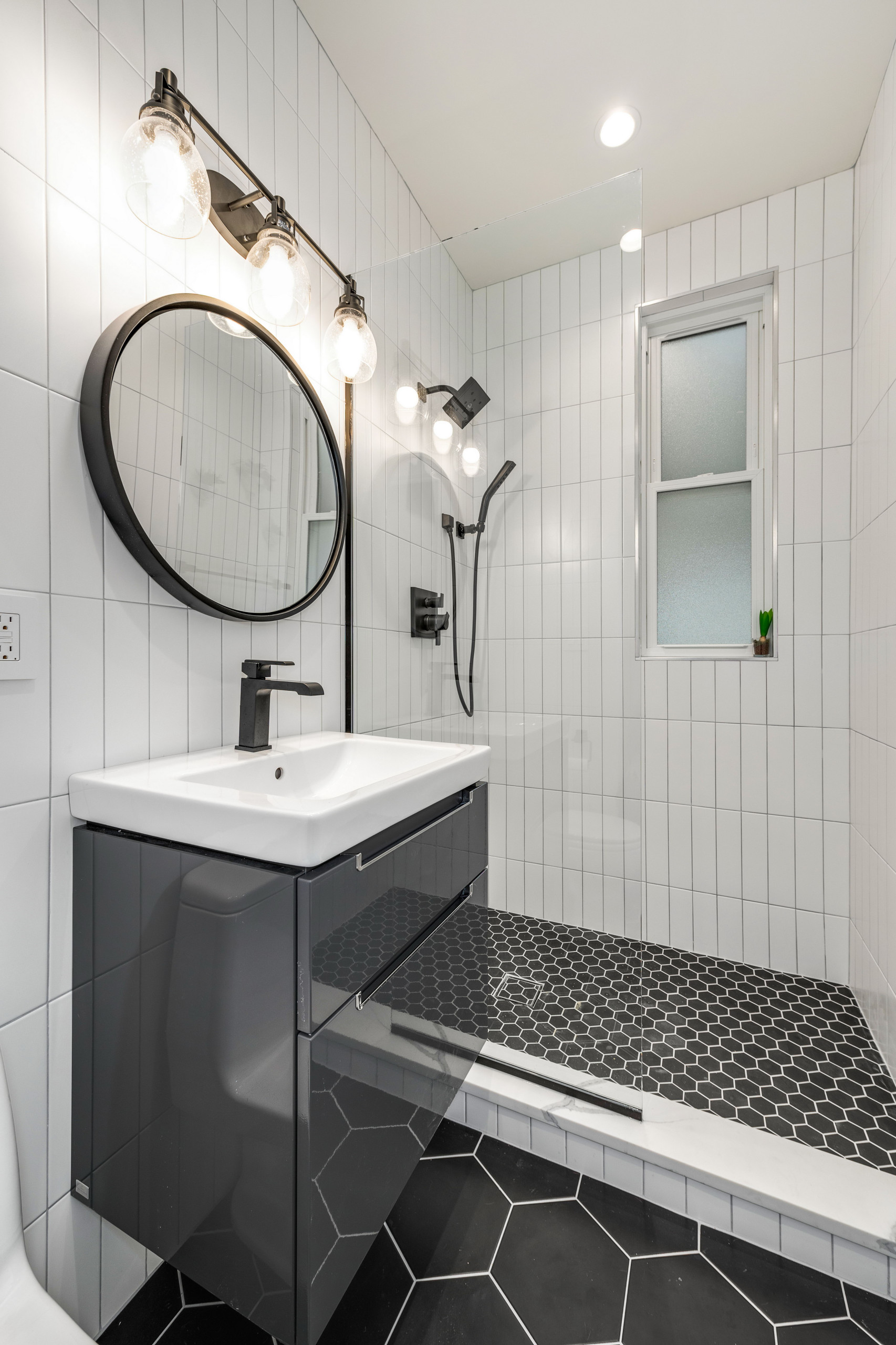 Modern bathroom with black and white tile design, floating vanity, and round mirror.
