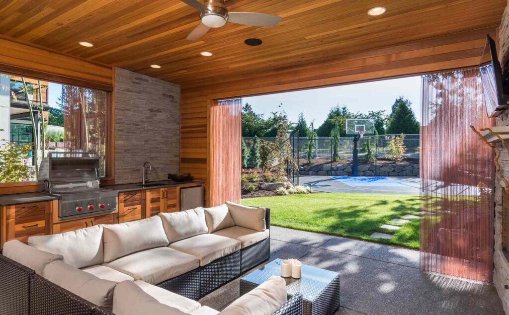 Covered patio with built-in grill, lounge seating, and view of backyard basketball court
