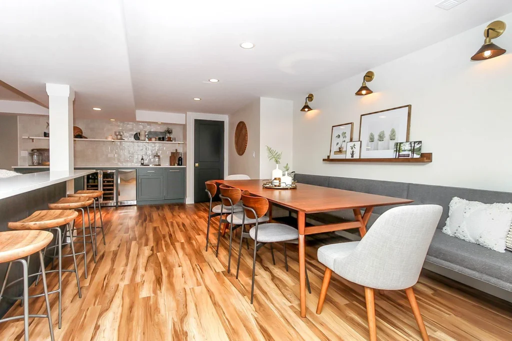 Basement remodel featuring wood floors, mid-century modern dining table with bench seating, and a sleek wet bar