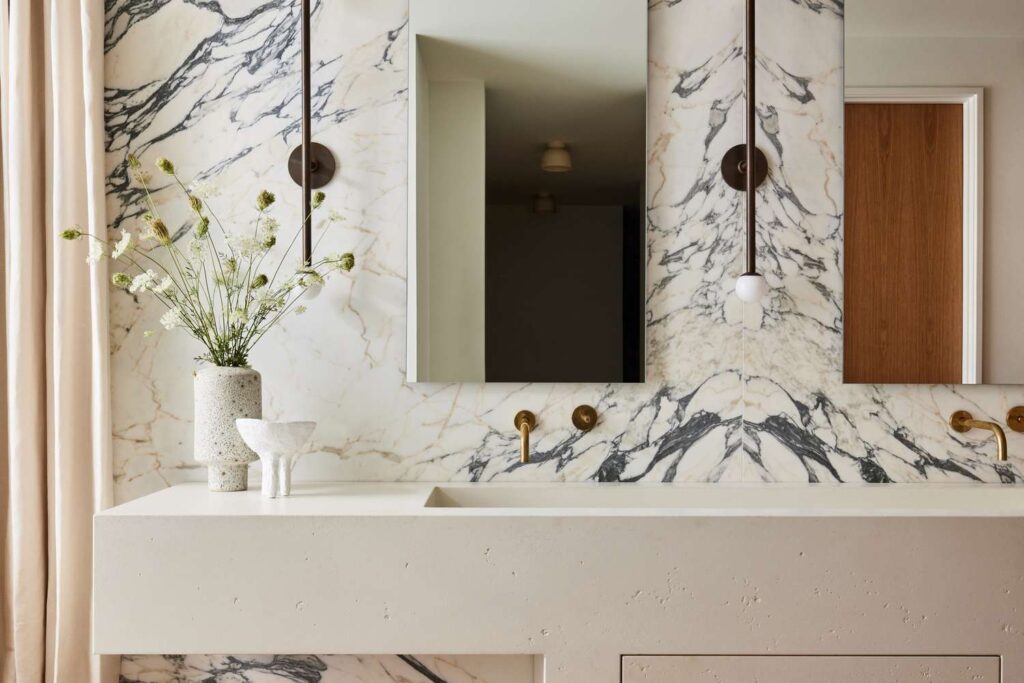 Modern bathroom with bold marble wall, floating concrete vanity, gold fixtures, and pendant lighting