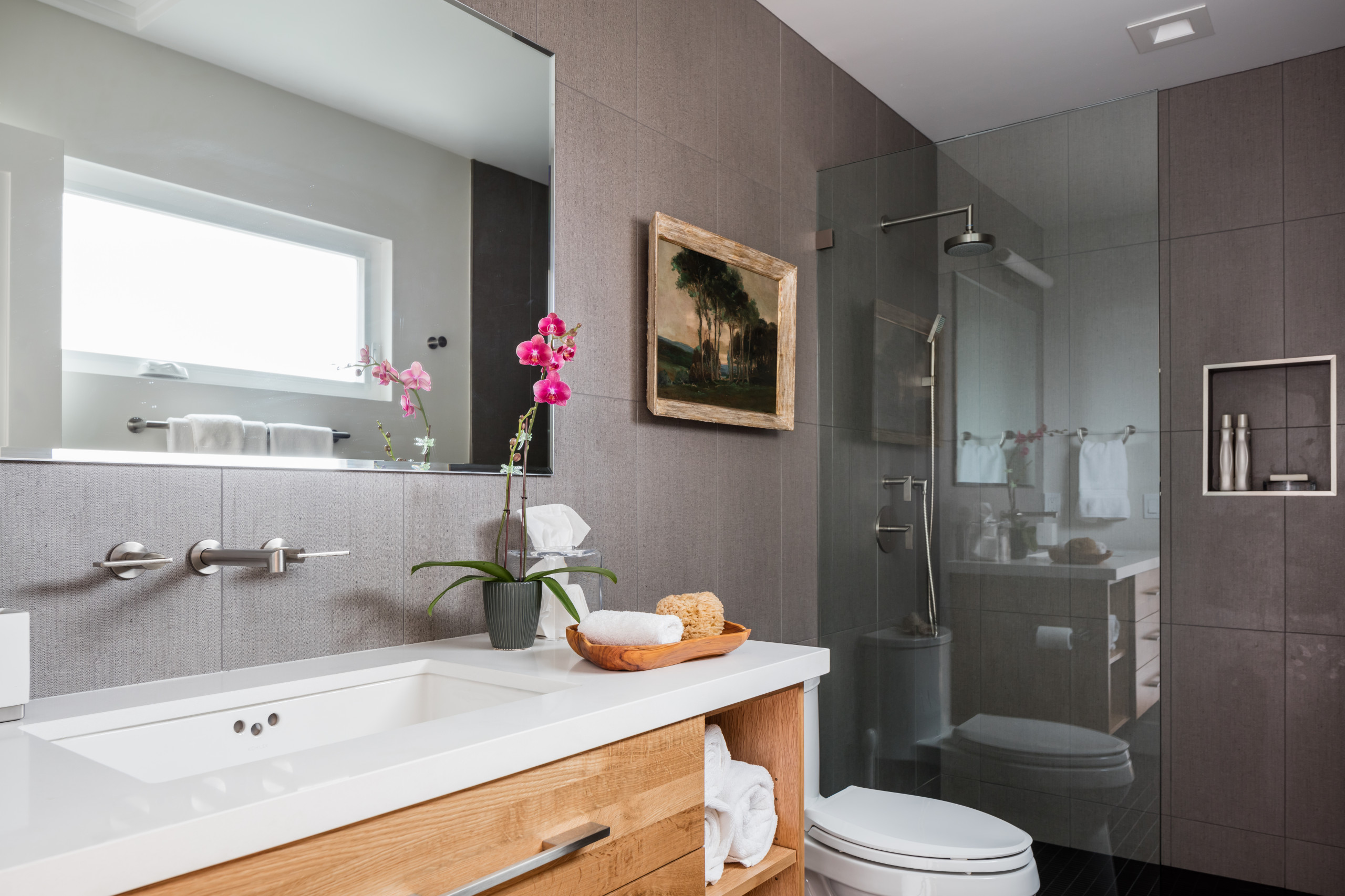 Modern bathroom with wood vanity, large mirror, and glass shower enclosure.