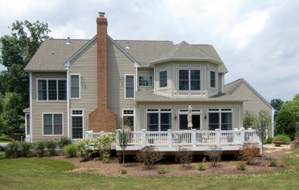Two-story house with large rear addition, brick chimney, multiple windows, and a white raised deck