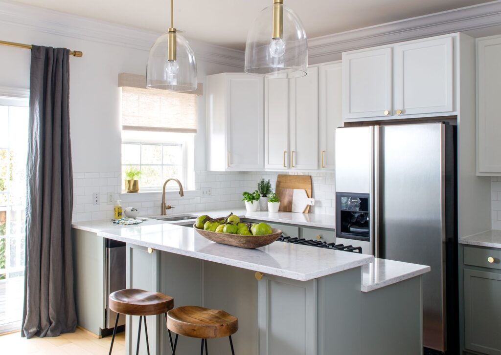 Bright kitchen with white cabinets, marble countertops, brass fixtures, and wood stools at the island