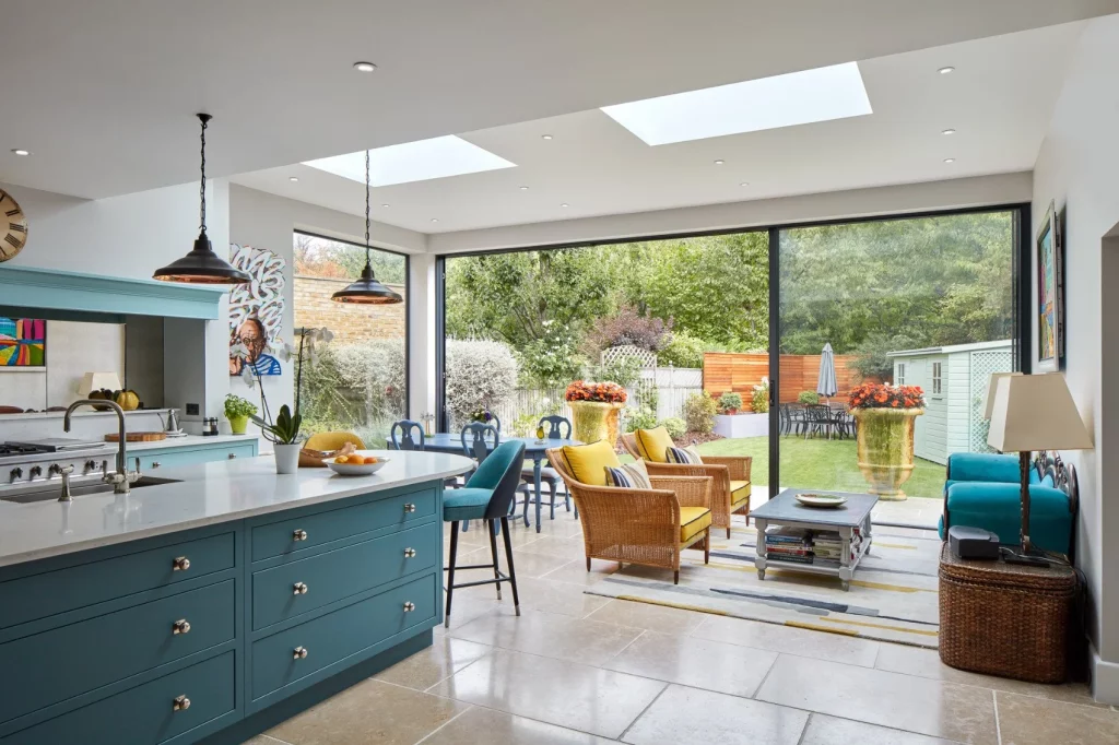 Bright kitchen extension with skylights, blue cabinetry, and large glass doors opening to a colorful garden.