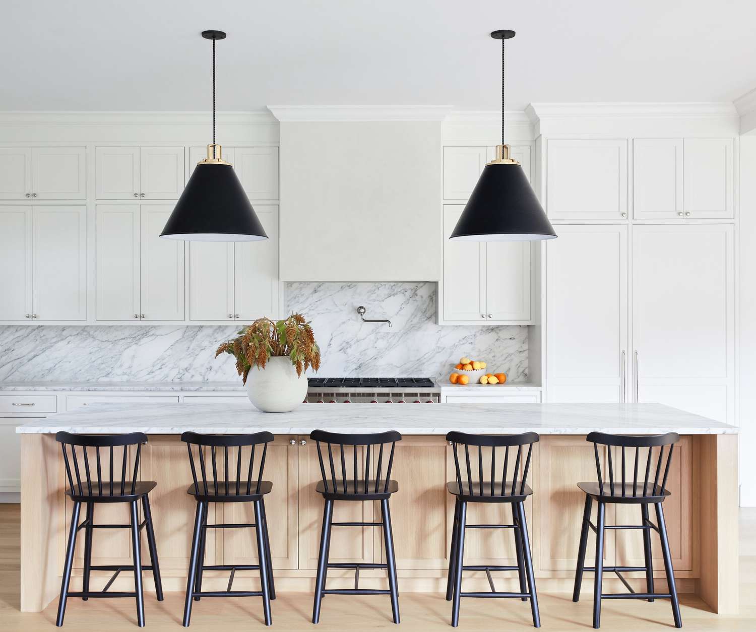 Minimalist kitchen with white cabinetry, marble backsplash, and a large island with black bar stools.