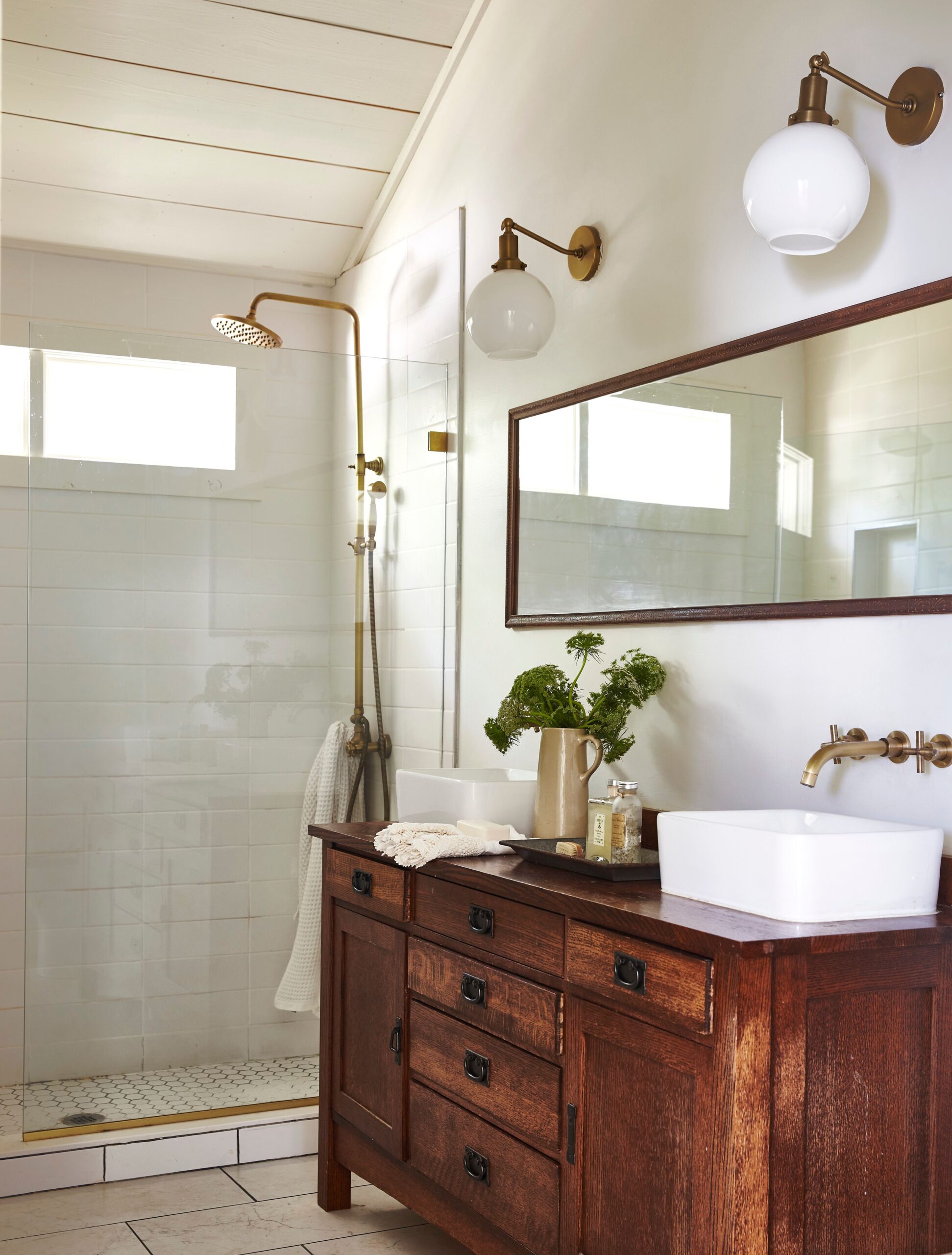 Bathroom with vintage wooden vanity, brass fixtures, and walk-in shower.