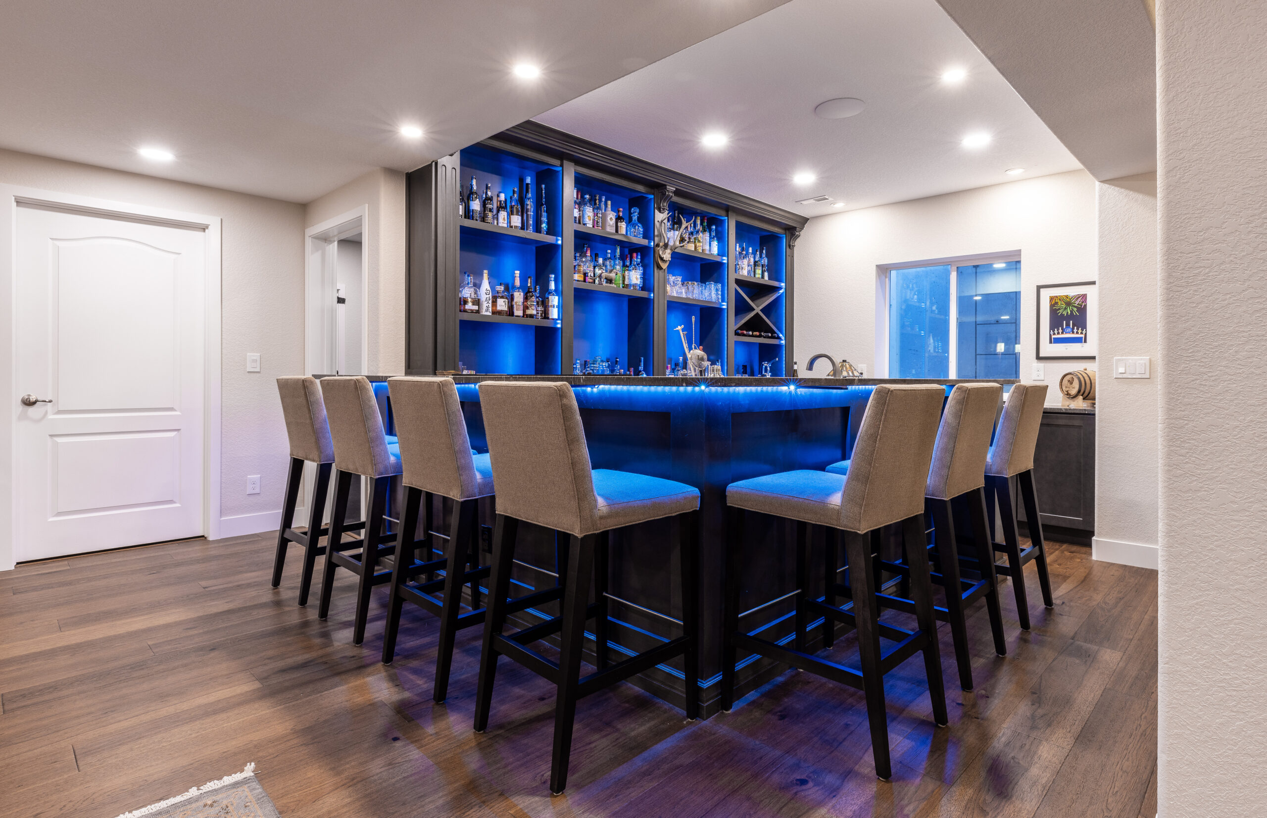 Modern home bar with illuminated blue shelves and high chairs.