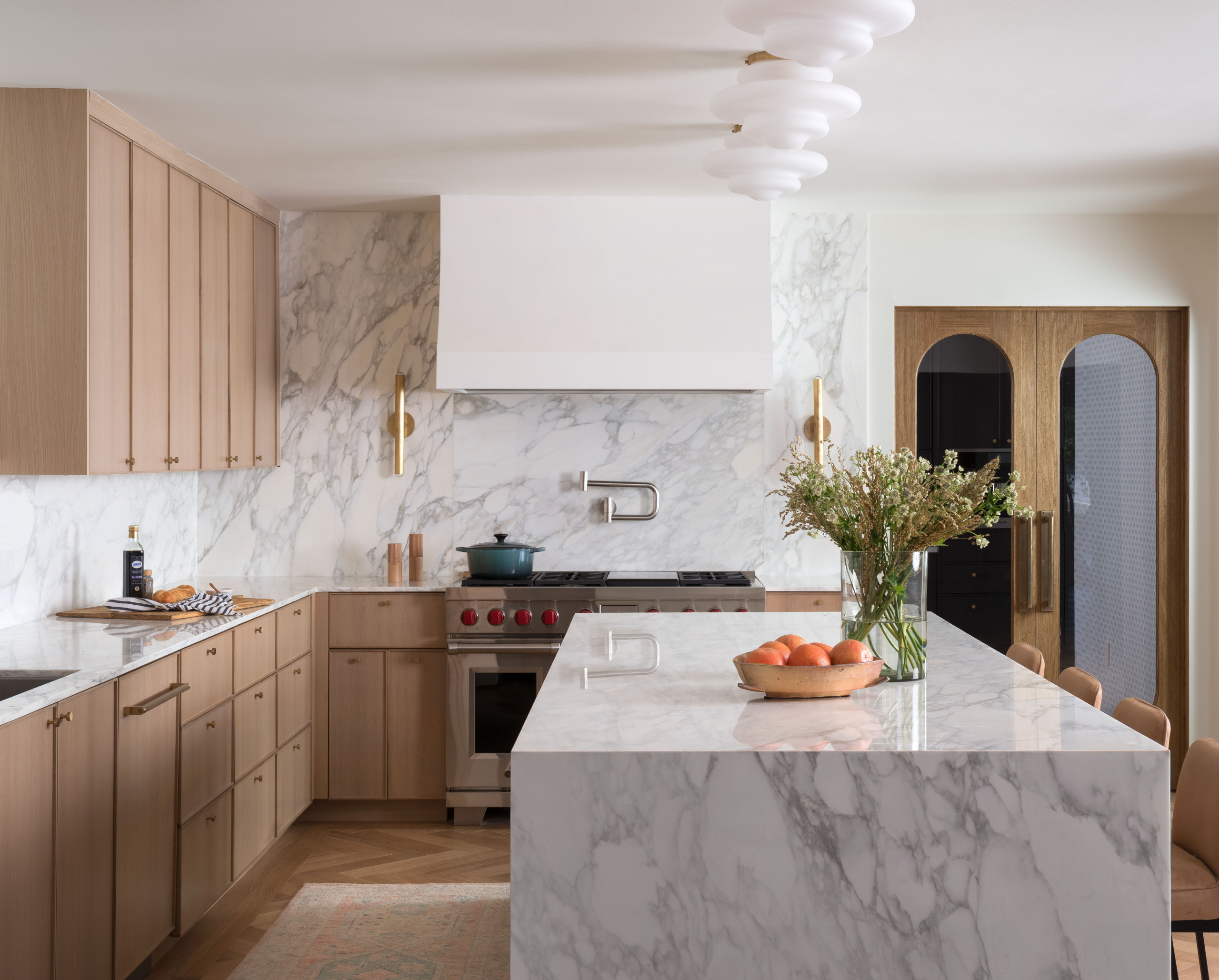 Modern kitchen with light wood cabinets, white marble surfaces, and gold accents.