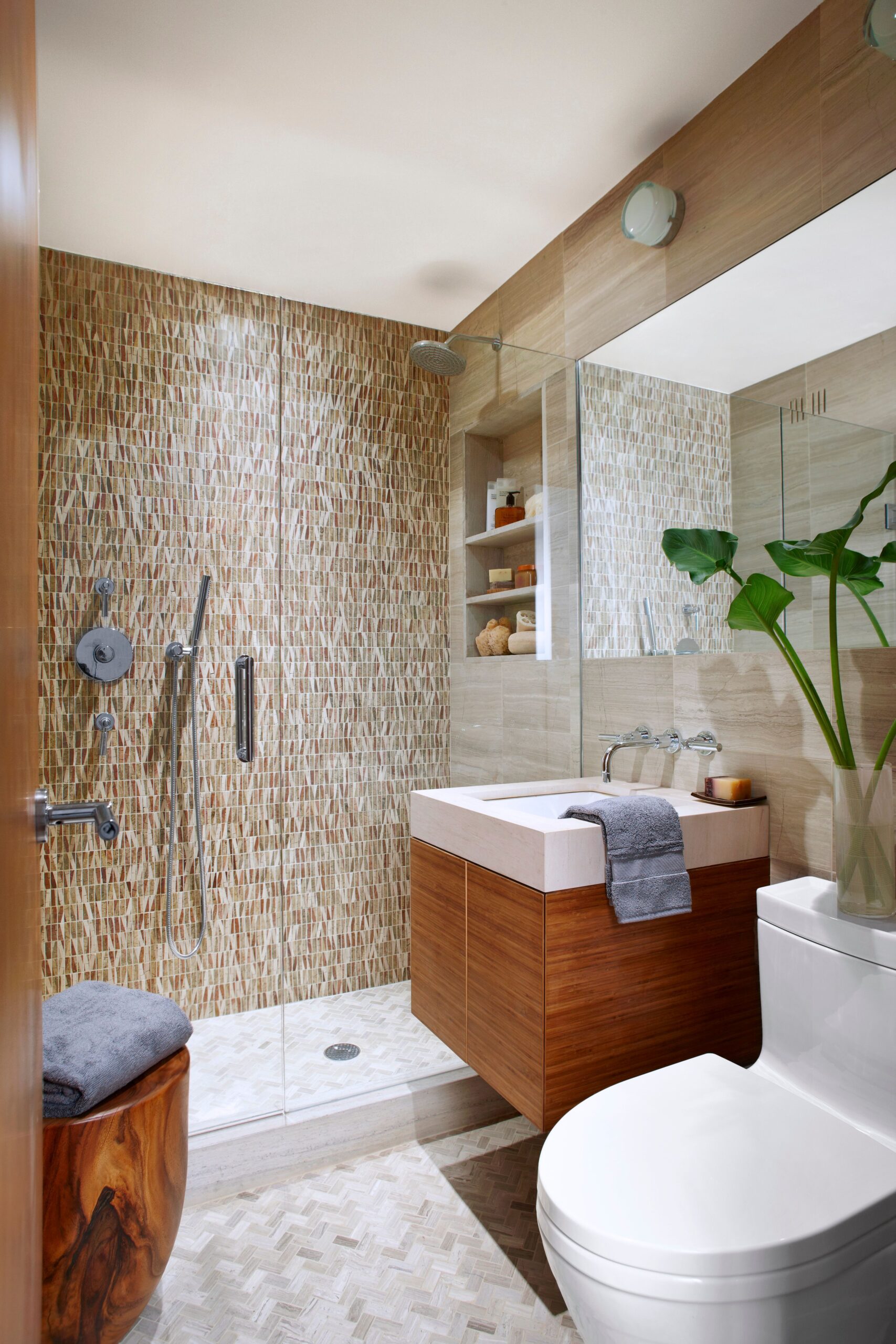 Modern bathroom with mosaic tile shower wall, floating wood vanity, and white fixtures.